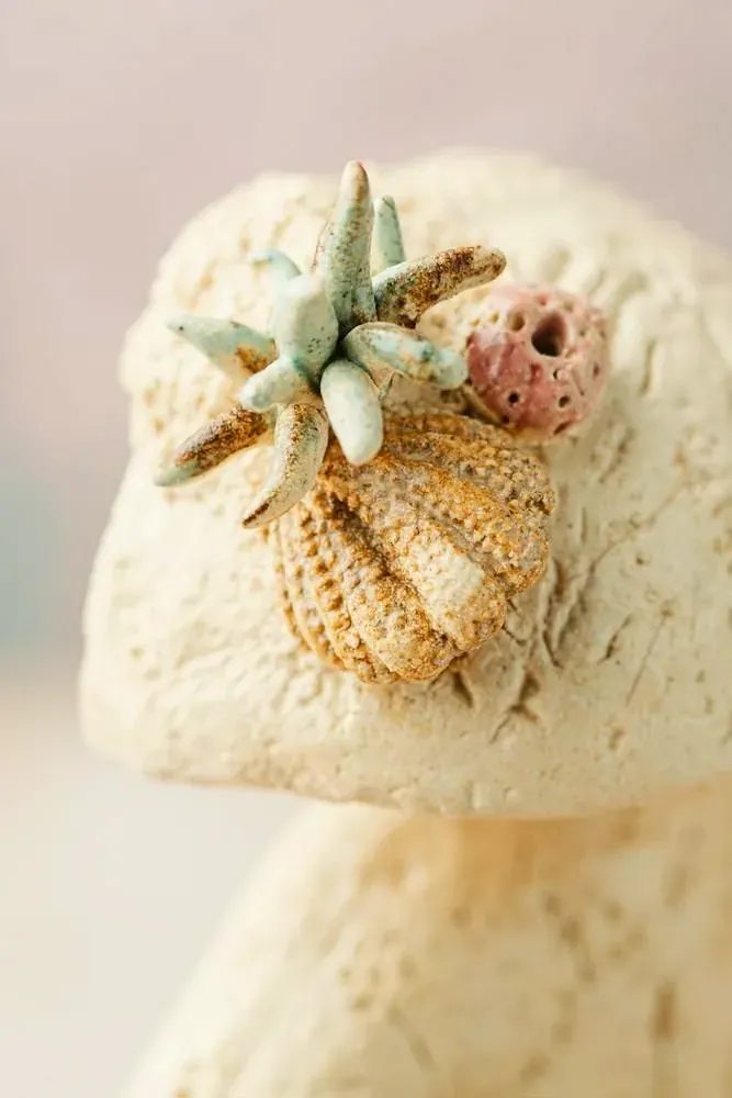Detalle del tocado: una estrella de mar, una concha y un coral rosa modelados sobre el gres
